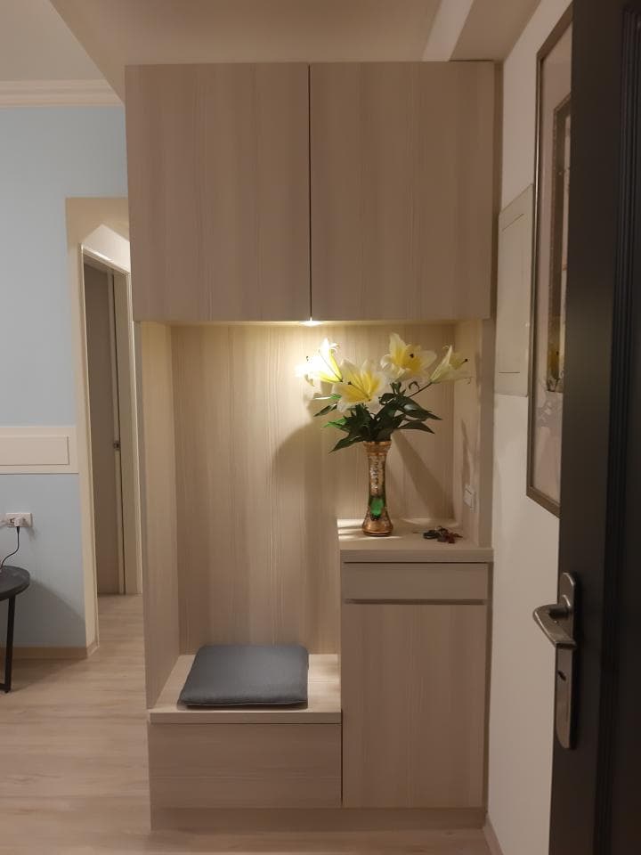 1) 照片中展示了一个木制鞋柜,鞋柜上有两个柜门和一个抽屉,抽屉上面放着一个花瓶,花瓶里插着花,鞋柜的下方有一个可以坐下的长方形垫子