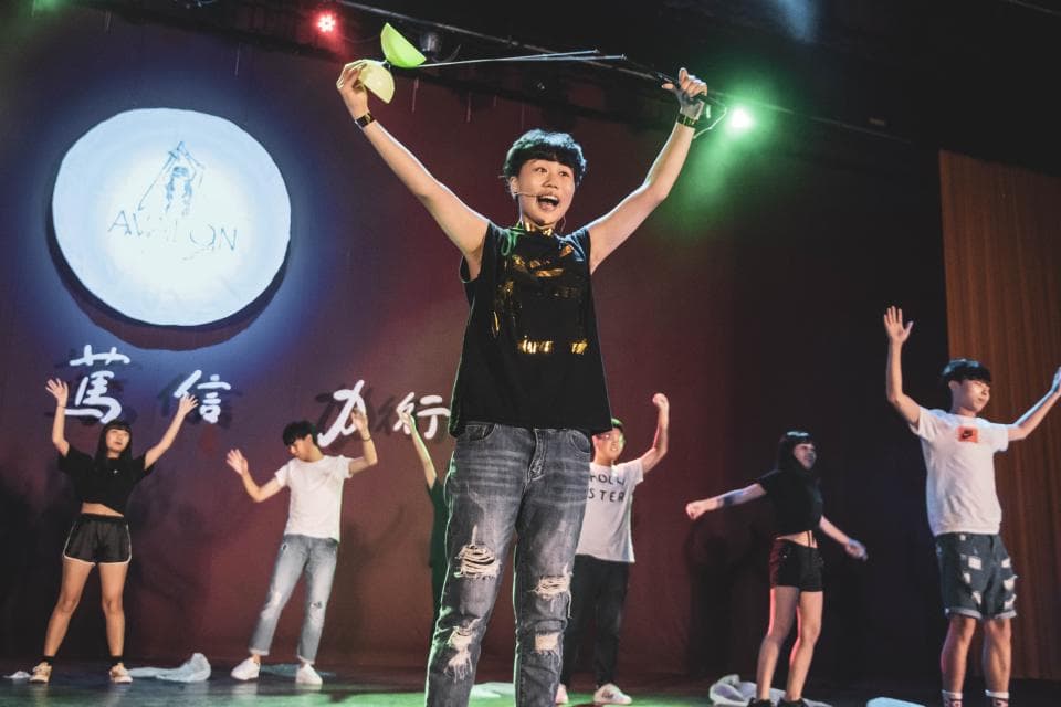 這張「表演」的照片是幾位年輕人在舞臺上表演,其中一位女生正在跳舞,其他人在臺下觀看。