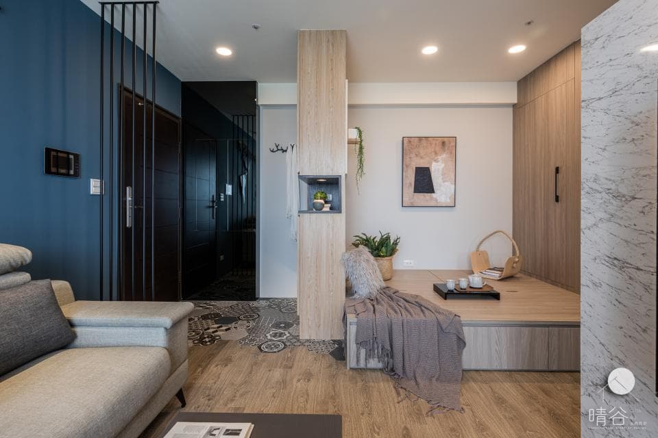 這張「室內設計」的照片是一個現代化的客廳,有藍色的牆壁、木質地板、以及一個可以坐著休息的平臺。平臺上有一個灰色的毯子,看起來很舒服。牆上還掛著一幅畫,為空間增添了一些藝術感。