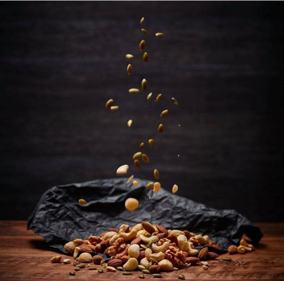 這張照片是一堆散落在黑色布料上的堅果,包括杏仁、核桃、腰果和南瓜子。