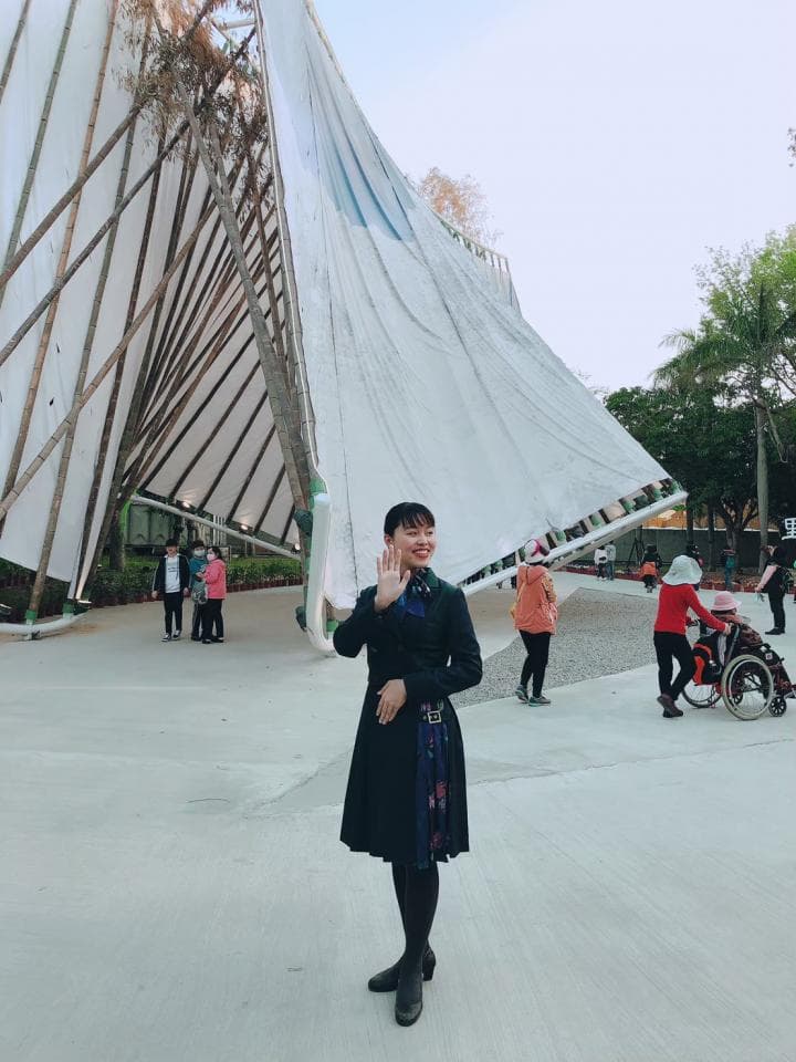 這張「建築物」的照片是一座巨大的白色帆布結構,中間有一位女性站在前面,她穿著黑色外套和格紋裙,背景有一些其他遊客。