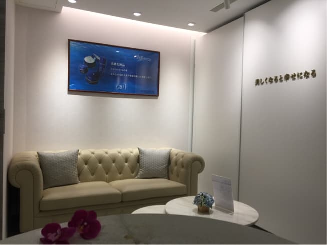 這張「美容診所等候區」的照片是一個白色簡潔的空間,牆上有金色字體的店名,還有沙發、茶几和花瓶。