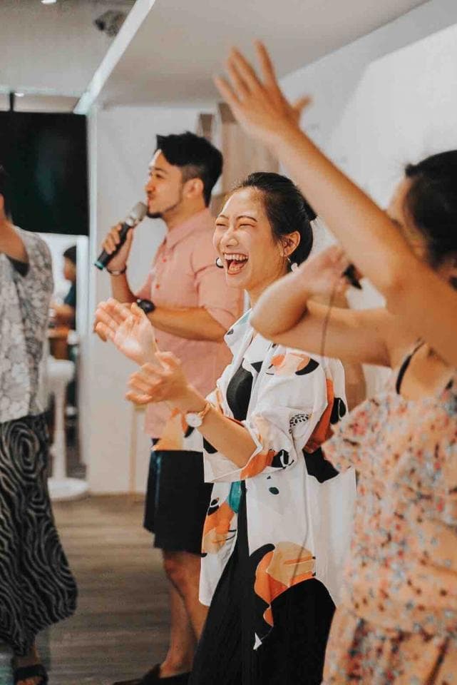 這張「一群朋友唱歌」的照片是,三位朋友在室內一起唱歌,其中一位朋友手持麥克風,另一位朋友笑得很開心。