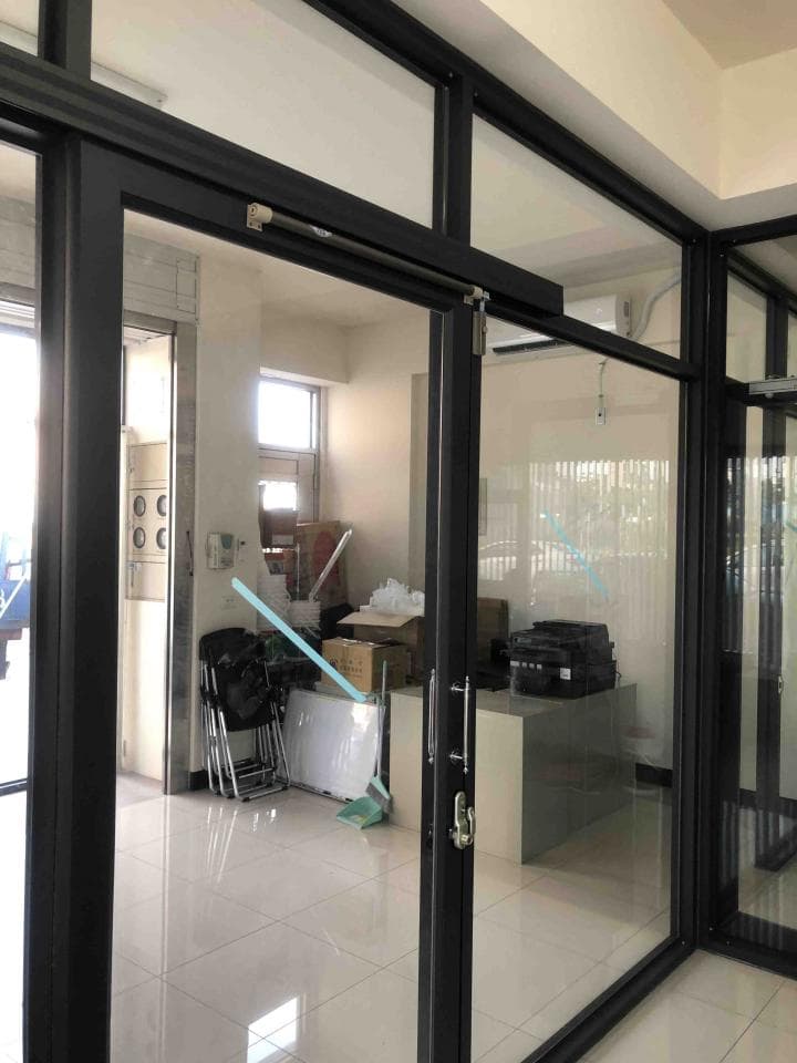這張照片是一間辦公室,其中最重要的是一扇黑色的玻璃門,門上有一個黑色的把手。門的另一邊可以看到一個辦公桌和一個椅子。