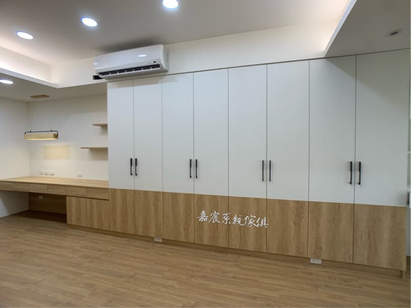 這張照片是一間房間,房間裡有一組大型的白色櫃子,櫃子下方是木質的,並配有黑色把手。