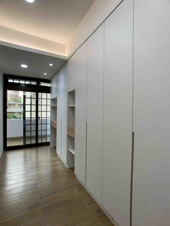 這張照片是一間現代化的臥室,最顯眼的是牆壁上的白色大型衣櫃,櫃門採用簡約的設計,沒有明顯的把手,呈現出簡潔俐落的視覺效果。