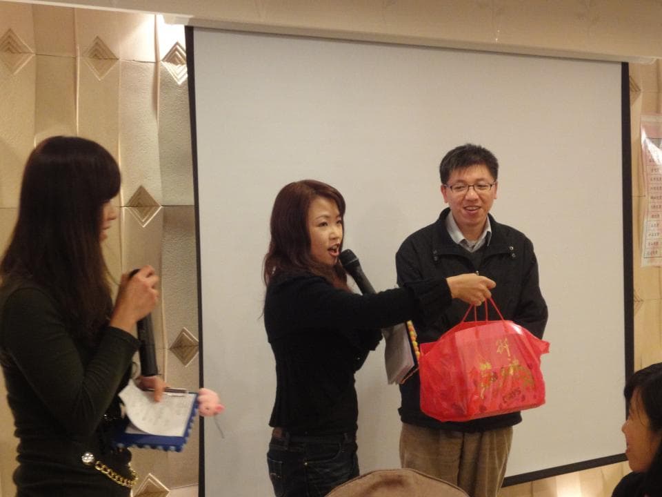 這張照片是三個女人正在一個房間裡,其中一個女人拿著一個紅色禮物盒,另一個女人拿著麥克風,第三個女人在聽她們說話。