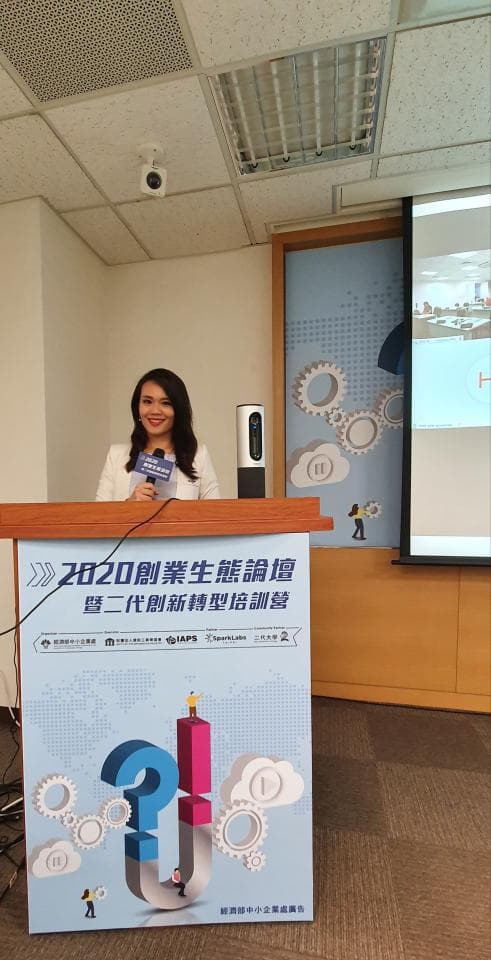 這張照片是 一位女性站在講臺上,她正在演講,講臺上面有寫著 2020創業生態價值暨第二代新媒體趨勢論壇 的標語。
