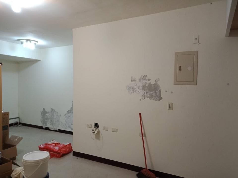1) 照片顯示一個正在裝修的房間,房間裡有刷新的白牆、天花板、地板和一些家具,牆上還有電線、開關和一個電箱