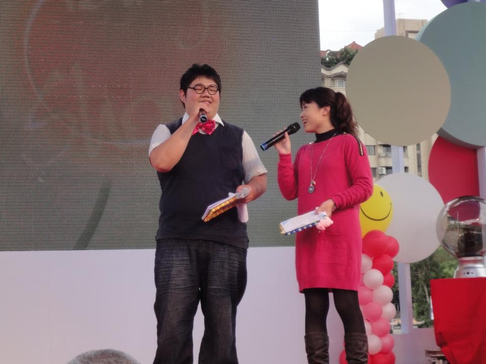 這張「舞臺活動」的照片是兩個主持人正在臺上說話,他們都拿著麥克風,旁邊還有許多氣球裝飾。