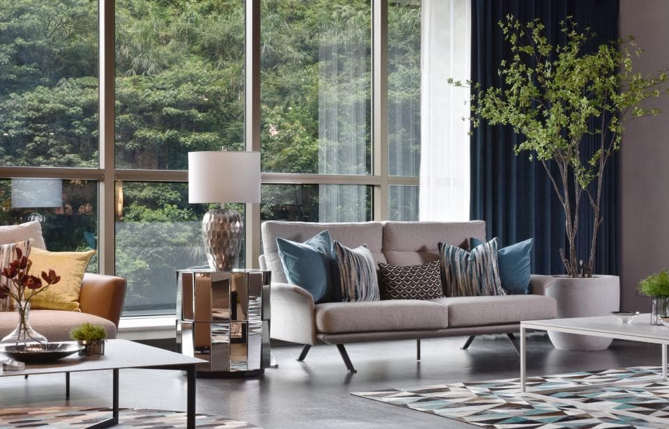 這張「客廳」的照片是一個舒適的空間,裡面有一張灰色的沙發,靠著大窗戶,窗外是綠樹和藍天。沙發旁有一個銀色的茶几,上面有一盞檯燈。