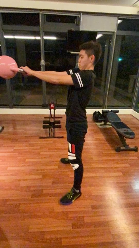 這張照片是一個年輕人在家裡舉著一個粉紅色的壺鈴做運動。