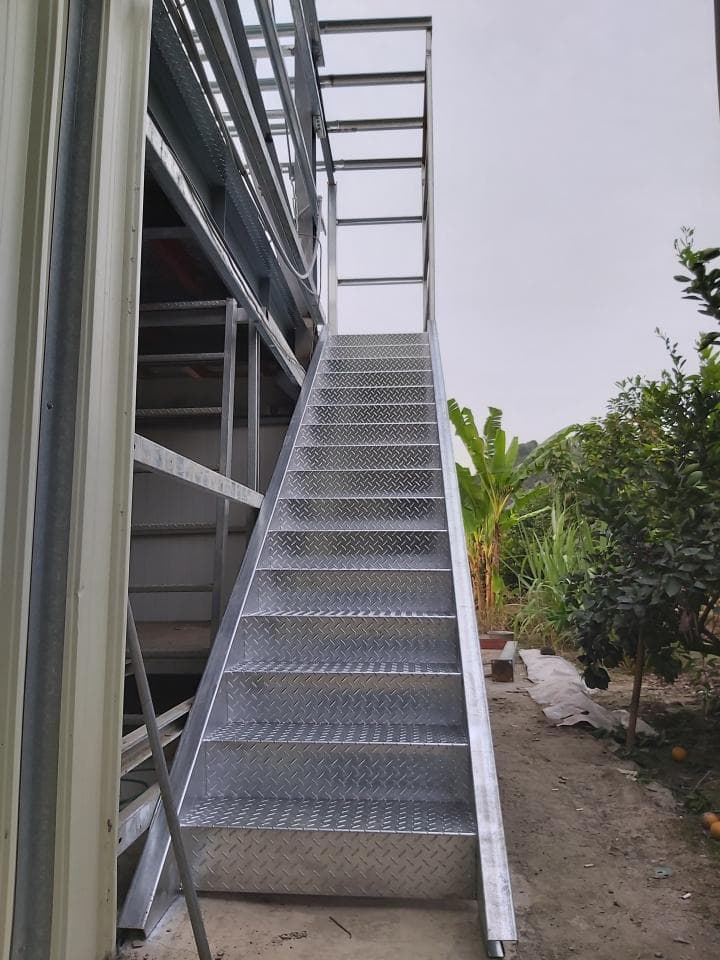 1) 照片顯示一棟建築物外側的鋼製樓梯,樓梯由金屬製成,並帶有防滑的鑽石形狀的紋路