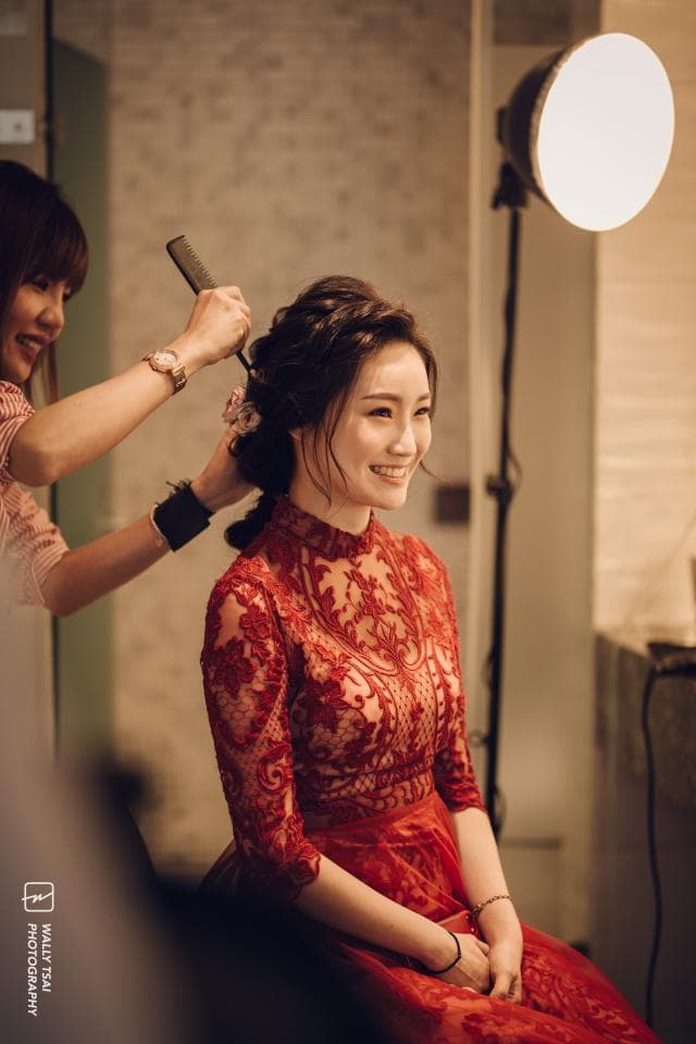 這張照片是一個穿著紅色蕾絲禮服的女孩,她正在接受髮型師的打理。