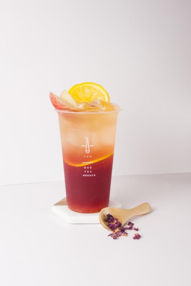 這張「水果茶」的照片是一杯裝滿水果茶的透明杯子,上面放了一片檸檬,杯子旁邊放了一個小木勺和一些玫瑰花瓣。