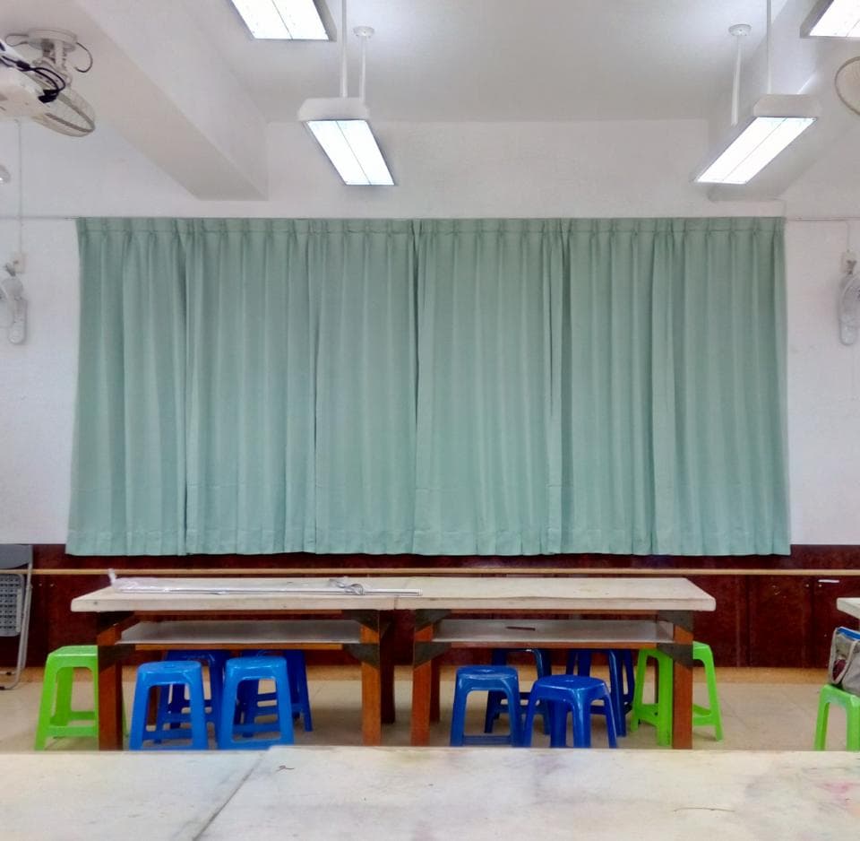 1) 照片顯示一間教室,教室裡有綠色的窗簾、木頭桌子、以及藍色和綠色的塑膠椅子