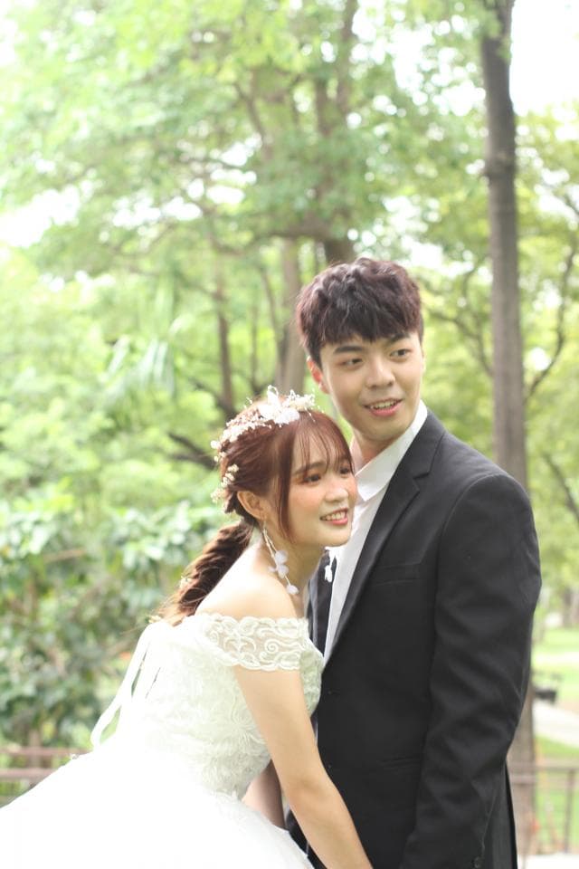 這張照片是一對新人在綠意盎然的公園裡拍攝婚紗照,新娘穿著優雅的婚紗,新郎則穿著合身的西裝,兩人相依偎在一起,畫面充滿甜蜜與幸福。