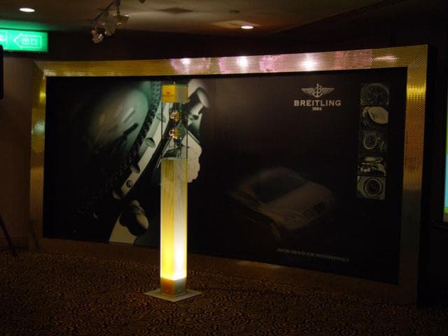 這張「佈置展覽」的照片是一間展覽場地,裡頭展示了汽車、手錶,以及一盞燈。