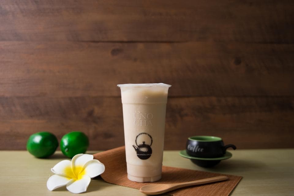 這張「奶茶」的照片是一杯裝滿奶茶的透明杯子,旁邊有一片綠葉,還有一隻木勺子。