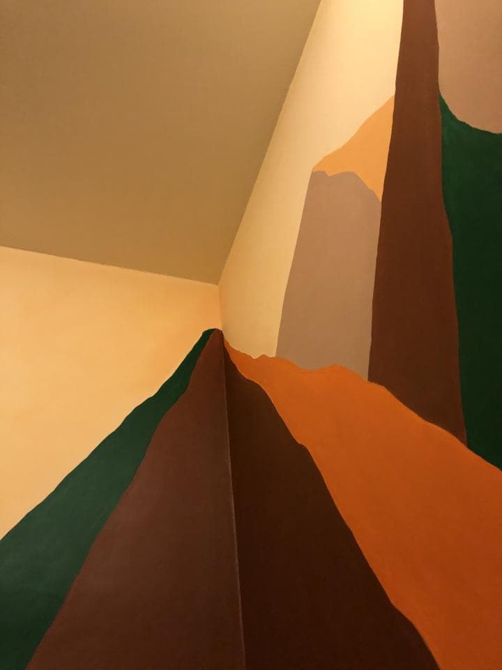 這張照片是一間牆壁上繪製了抽象山脈圖案的房間。房間的牆壁以大地色系為主,呈現出層層疊疊的山峰,使空間充滿自然和寧靜的氛圍。