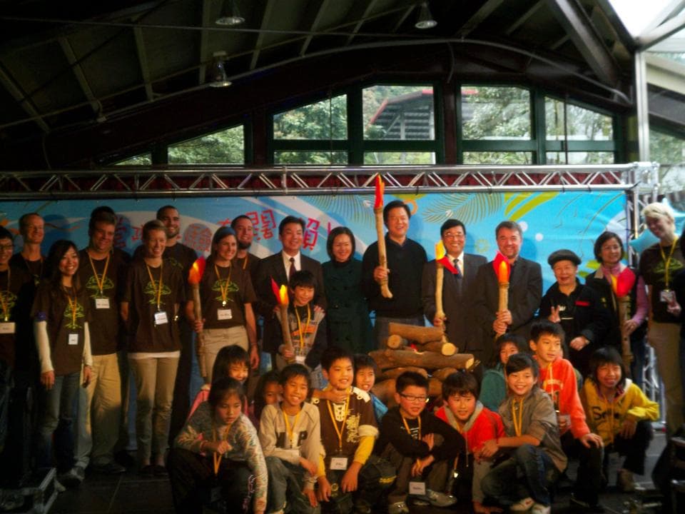 這張「一群人聚會」的照片是,一群人在戶外舉行活動,他們圍繞著一個裝飾著紅色和黃色燈光的地方,大家看起來很開心,有大人也有小孩。