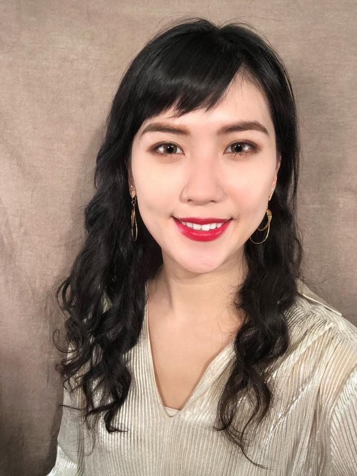 這張「一位年輕女性肖像」的照片是,她擁有烏黑亮麗的長捲髮,身穿米白色上衣,並戴著金色的耳環。