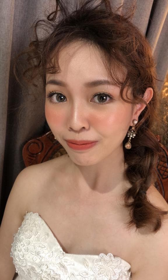 這張婚紗照是一位穿著白色蕾絲婚紗的女性,她擁有長捲髮,並戴著精緻的耳環。她面帶微笑,看起來很幸福。