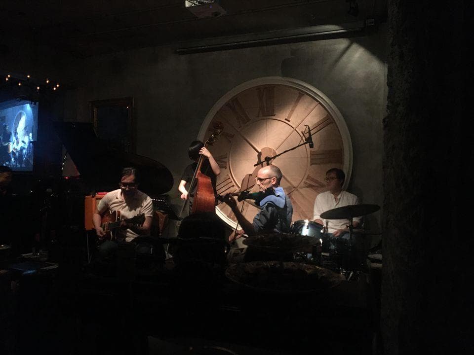 這張照片是一個樂隊在一個昏暗的房間裡演奏。他們在一個巨大的時鐘下演奏,時鐘是照片中最重要的部分。