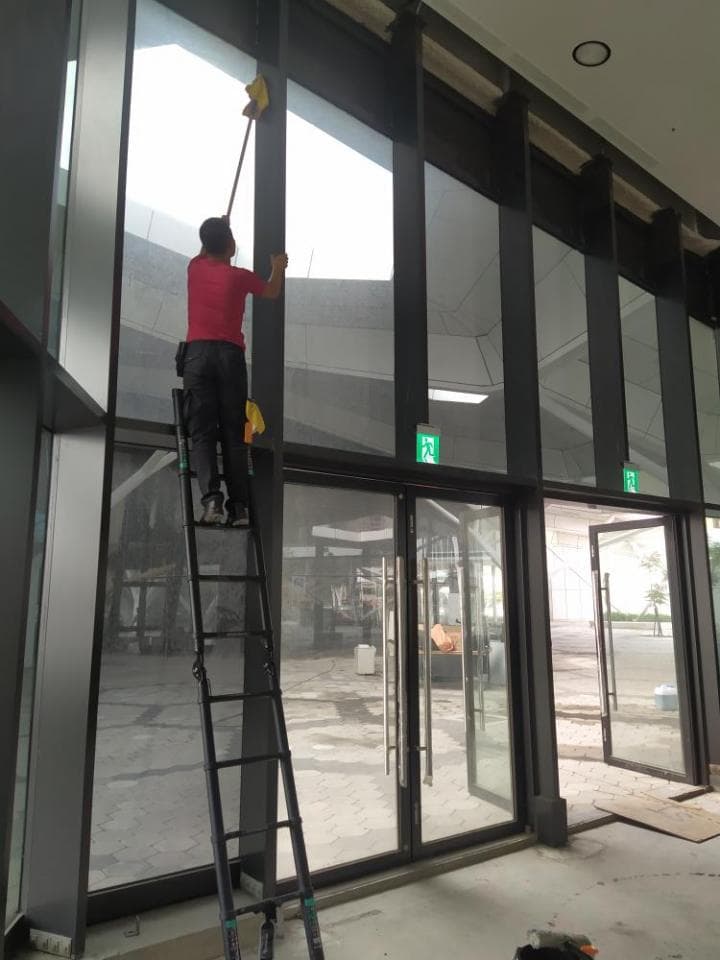 1) 照片顯示一名身穿紅色襯衫的男子站在梯子上,用抹布清潔大片玻璃窗