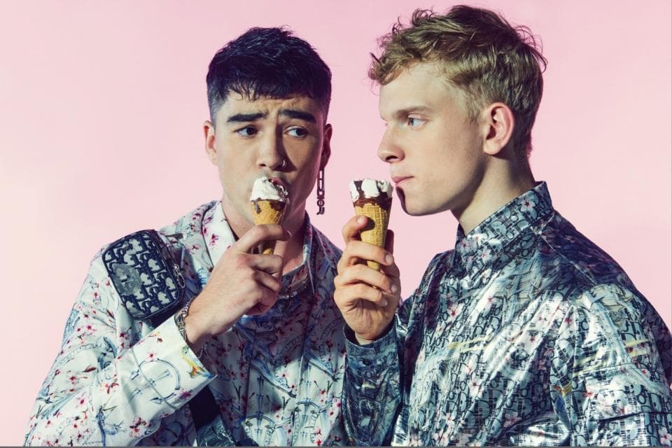 這張「兩個年輕人吃冰淇淋」的照片是:兩個年輕男子,一個穿白色印花襯衫,另一個穿銀色印花襯衫,他們都吃著冰淇淋。