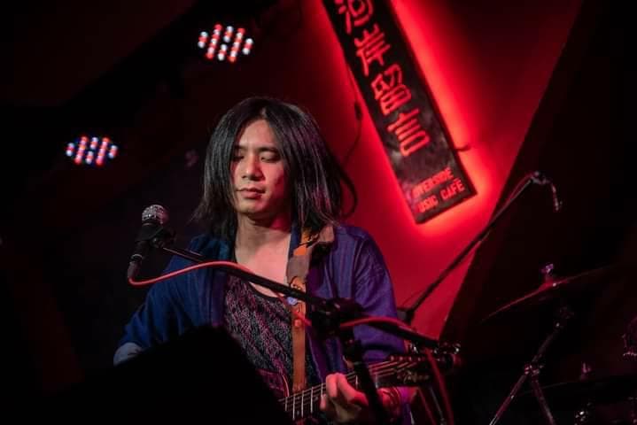 這張「音樂表演」的照片是一個在昏暗舞臺上表演的歌手,他拿著一把吉他,正唱著歌。舞臺上有一盞燈光,照亮了他的臉。歌手的背景是紅色的牆壁,上面寫著「音樂咖啡館」的招牌。