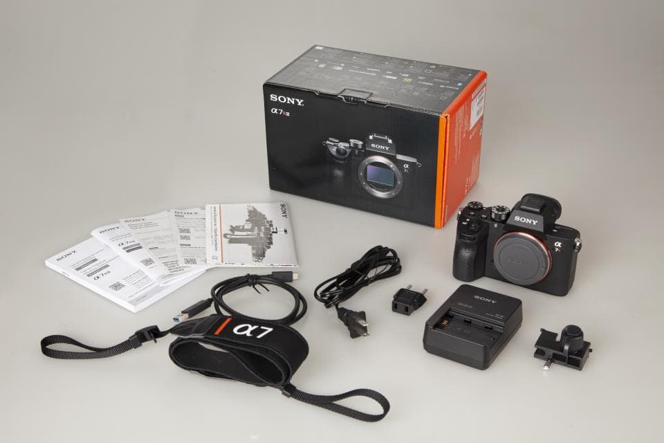 這張「索尼 α7 IV 相機」的照片是,一臺黑色的相機、一個相機袋、一個充電器、一個說明書和其他的配件。