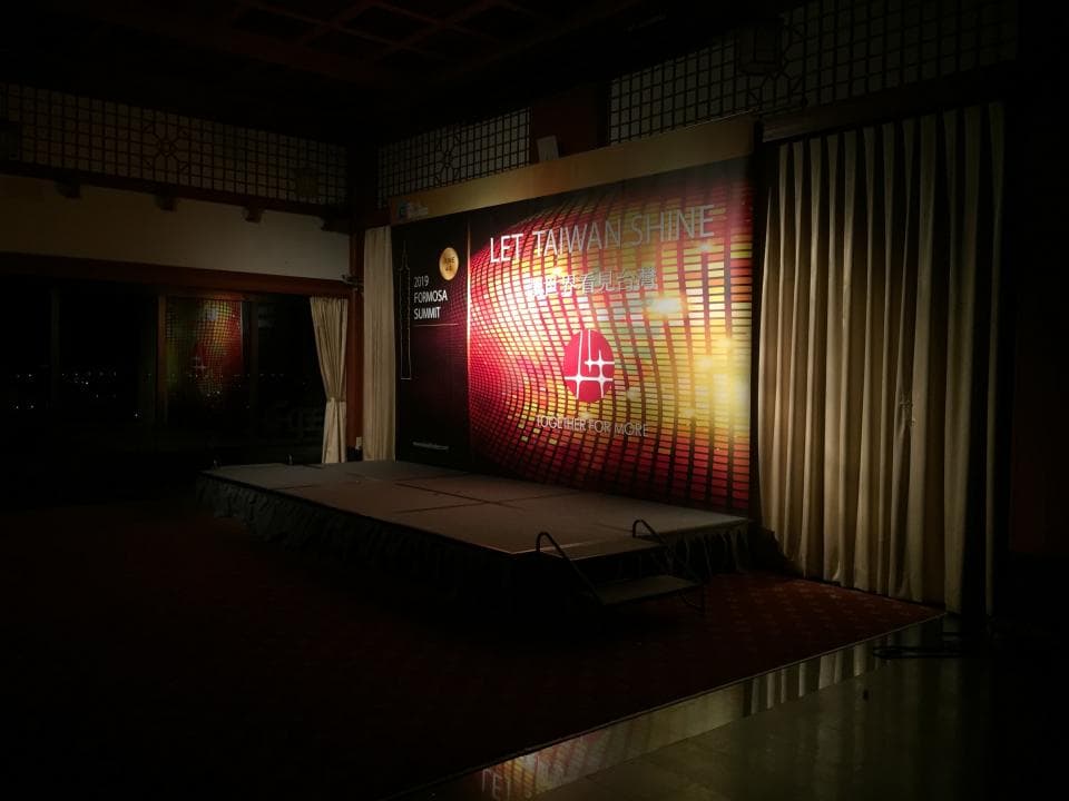 這張「舞臺」的照片是一個黑暗的房間,舞臺上有一個巨大的背景,上面寫著「LET TAIWAN SHINE」。舞臺上也有一些燈光和設備。
