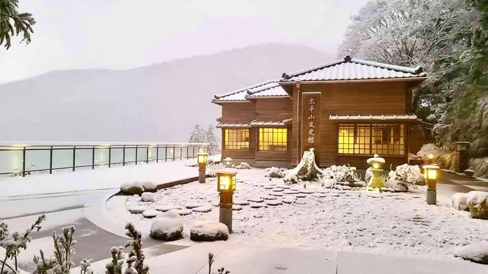 這張照片是一棟木造建築,屋頂上蓋著厚厚的積雪,看起來非常寧靜祥和。建築前方有幾盞燈,照亮了周圍的雪景,讓人感受到溫馨舒適的氛圍。