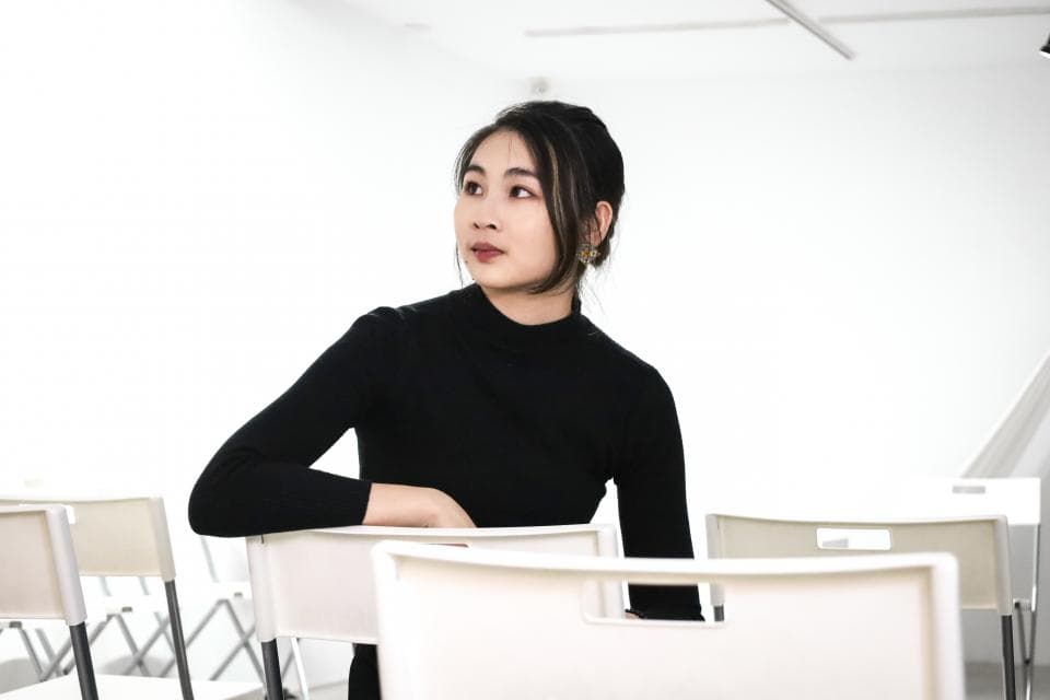 這張「年輕女子坐在白椅上,穿著黑色上衣,凝視著遠方」的照片是。