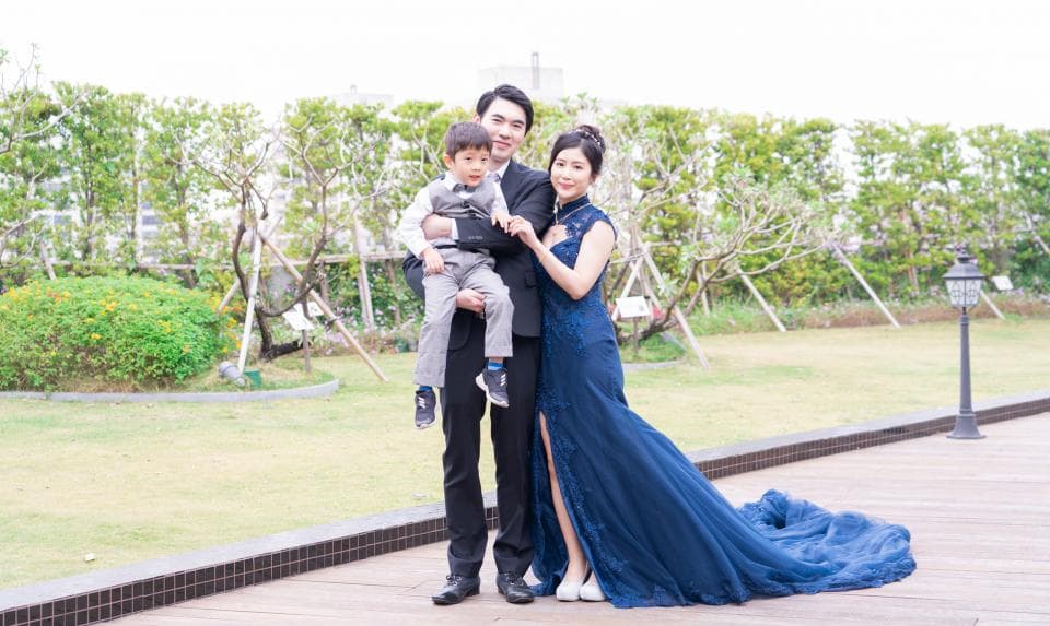 這張「一家三口」的照片是在戶外拍攝的,爸爸穿著西裝,媽媽穿著藍色禮服,兒子則穿著白色襯衫,他們一家三口站在一起,看起來非常幸福。