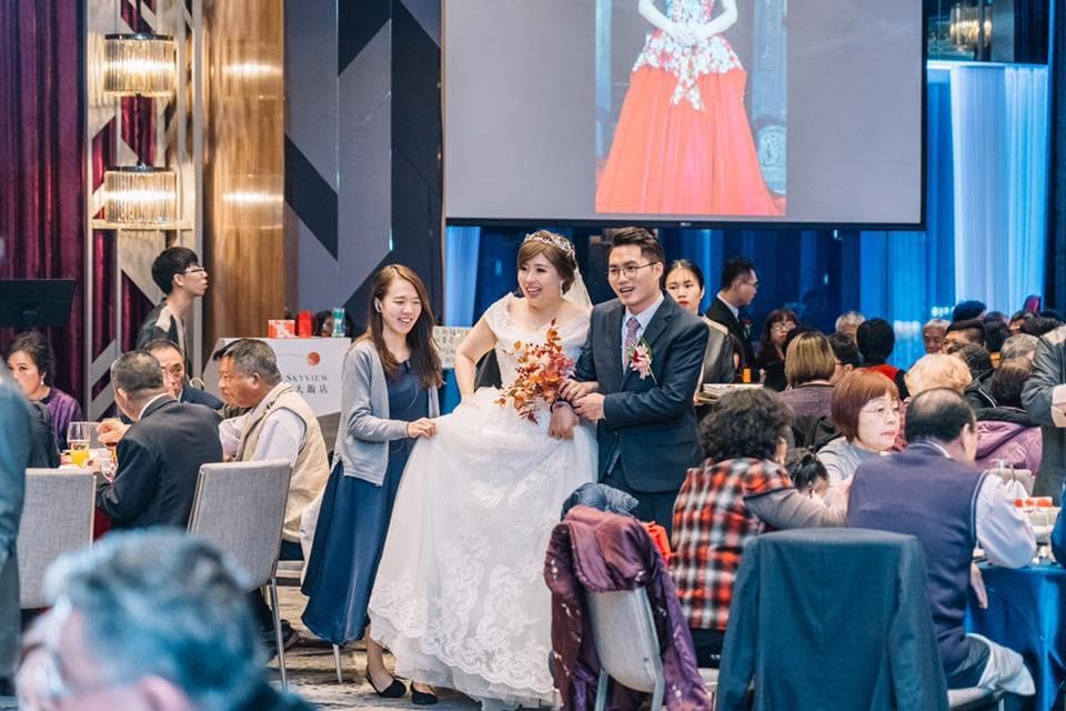 這張照片是一對新人正在舉行婚禮,新郎穿著黑色西裝,新娘穿著白色婚紗,他們站在臺前,笑容滿面,現場賓客都熱烈鼓掌,場面十分溫馨浪漫。