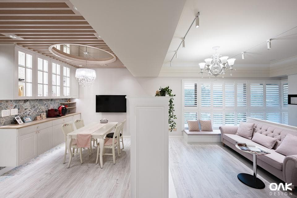 這張「客廳」的照片是一個明亮寬敞的空間,有著白色的木質地板、白色的牆壁和白色的傢俱。客廳裡有一張沙發、一個茶几和一個大窗戶,窗外是綠色的植物。牆上有一個嵌入式的櫃子,裡面裝滿了物品。客廳的天花板上有軌道燈和一個水晶燈。