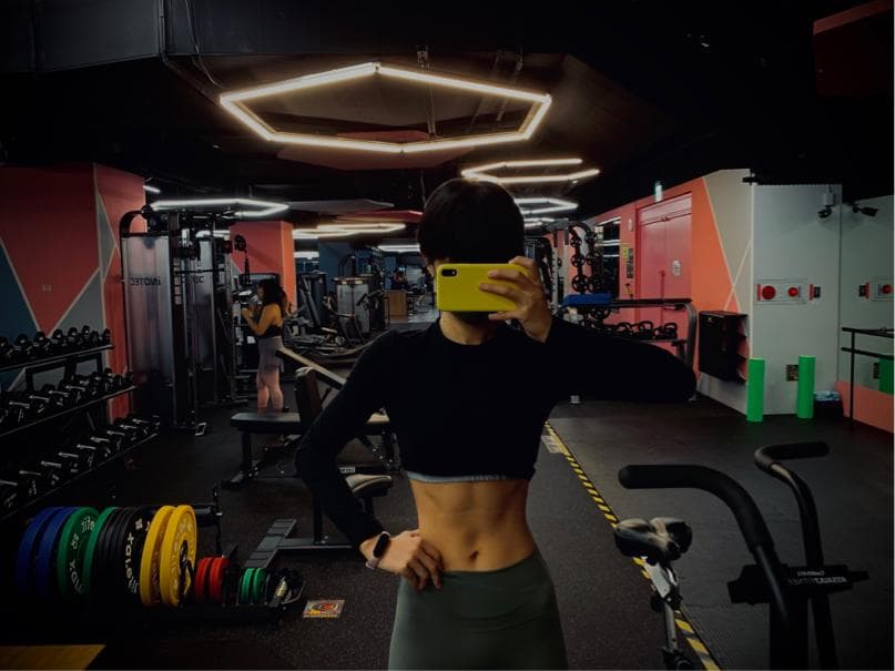 這張照片是一個健身房,照片的中心是一個年輕女人,她穿著黑色的運動服,正在健身房裡自拍。