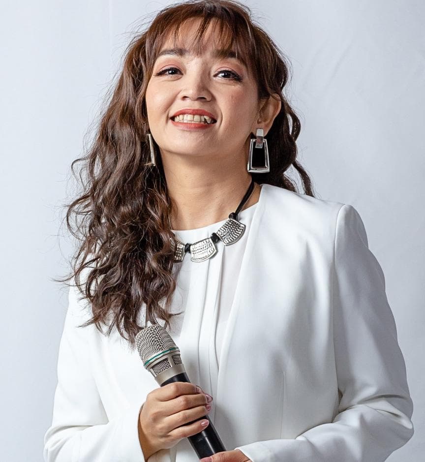 這張「一位女性拿著麥克風,穿著白色西裝外套,面帶笑容」的照片是。