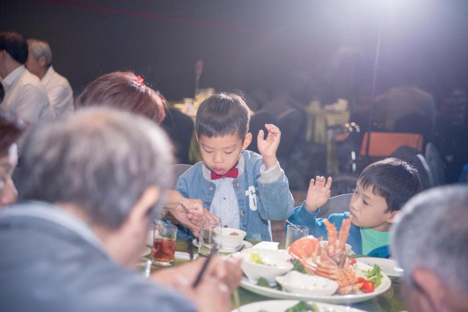 這張「一群人在餐桌上吃飯」的照片是,一個大人正在跟兩個小孩吃飯,他們桌上有一盤海鮮,旁邊還有飲料。