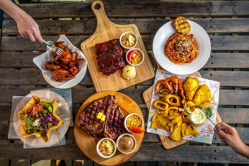 這張「美食」的照片是一張擺滿了各種食物的桌子,包括烤雞翅、烤牛排、烤豬肋排、義大利麵、薯條、沙拉和一些醬料。