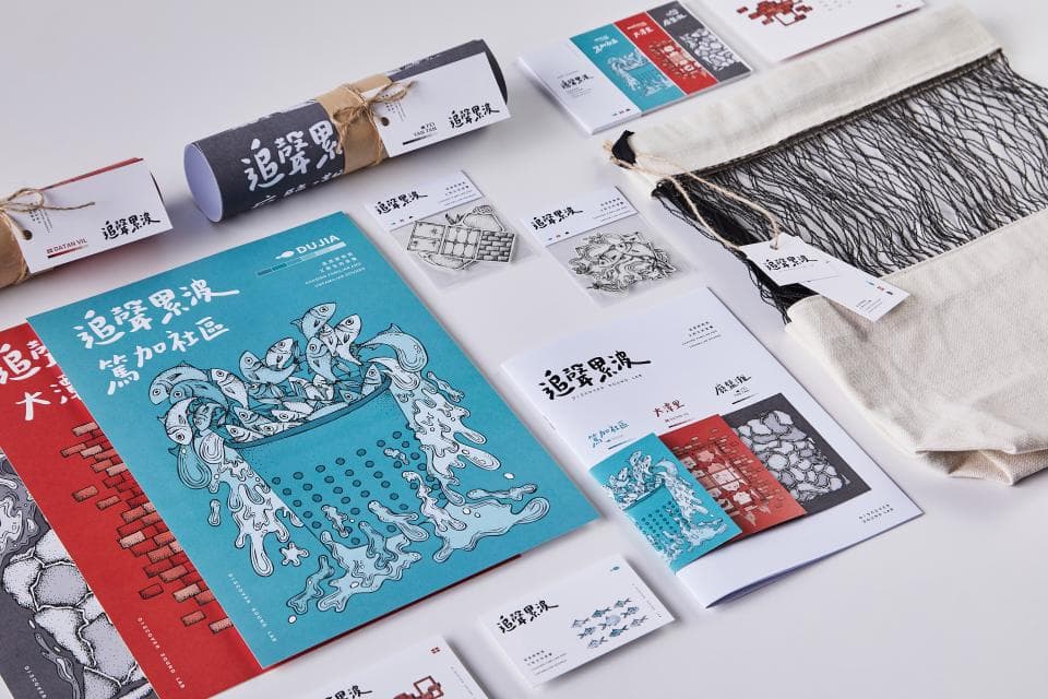 這張照片是充滿海洋元素的視覺設計,其中最重要的是一張藍色底色、以黑色線條繪製的插畫,描繪了滿滿的魚兒被裝進一個圓形的篩網中,周圍是藍色的水花,畫面充滿活力和動感。