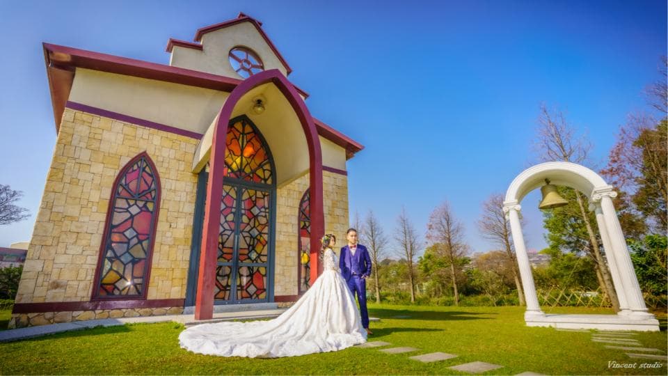 這張婚禮照片是一對新人站在教堂前,新娘穿著白色的婚紗,新郎穿著藍色的西裝。