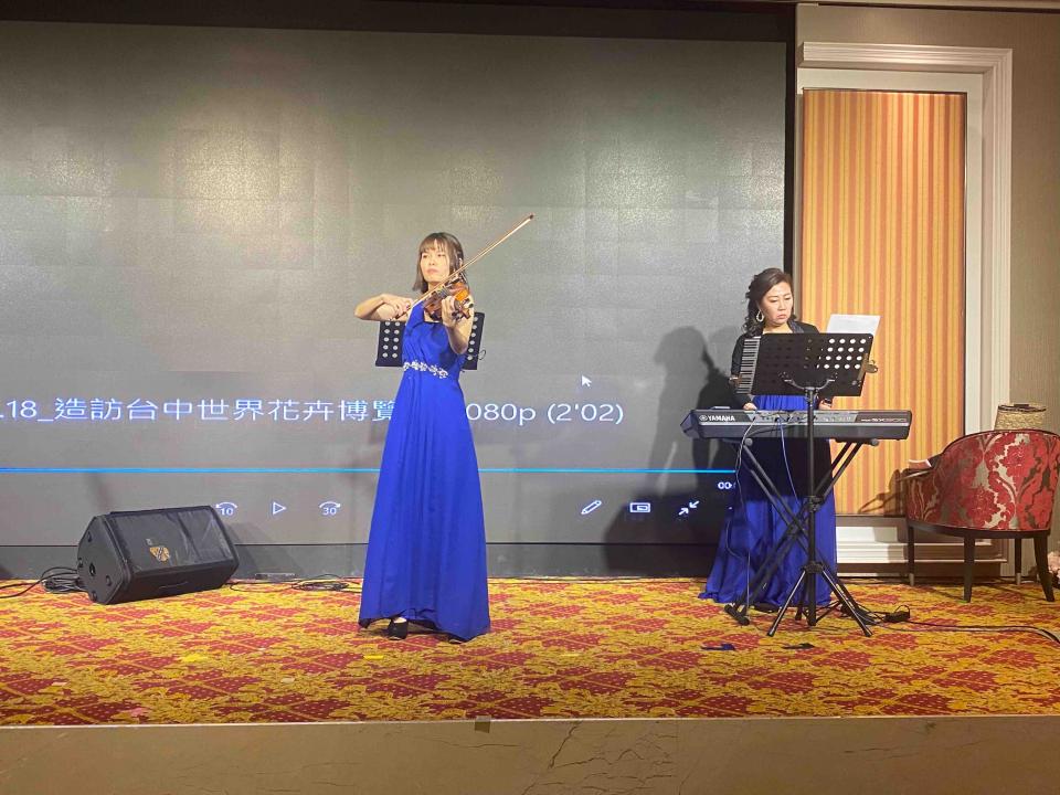 這張照片是兩位女性音樂家在舞臺上表演,一位演奏小提琴,另一位彈奏鍵盤。她們都穿著藍色的禮服,看起來很優雅。