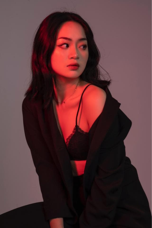 這張照片是一個穿著黑色外套的女孩,她留著黑色的短髮,她的臉上被紅色的燈光照亮,顯得格外迷人。