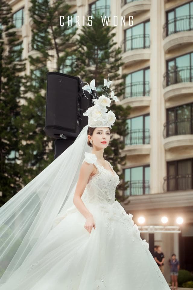 這張婚紗照是一個穿著白色婚紗的新娘,她戴著一個由花朵製成的頭飾,背景是一棟建築物。