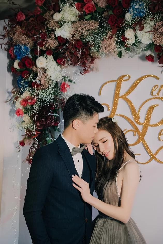 這張「婚禮」的照片是一對新人在一個佈置滿鮮花的背景前擁抱,新郎穿著西裝,新娘穿著禮服,他們看起來非常幸福。