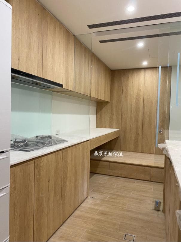 這張照片是一個現代化的廚房,木質的櫥櫃和桌面看起來很簡潔。右側有一個木質的餐桌和座位,方便人們在廚房用餐或工作。