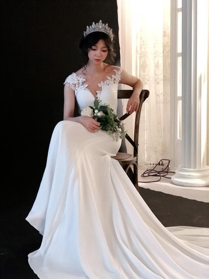 這張照片是一名穿著白色婚紗,戴著皇冠的新娘。她坐在一個木製的椅子上,手裡拿著一束白色的花束。